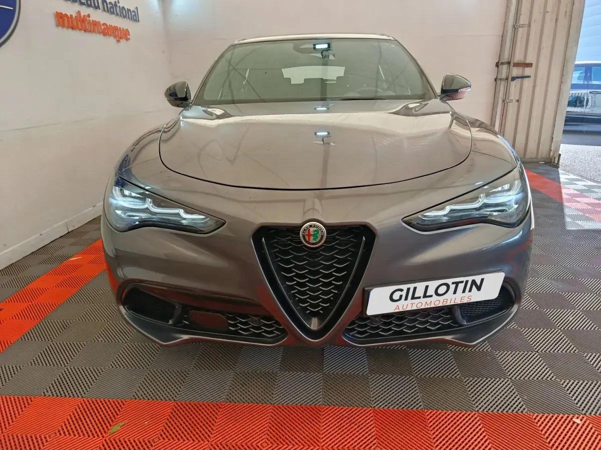Vue frontale d'un Alfa Romeo Stelvio gris foncé 2024 avec calandre en V et phares LED allumés.