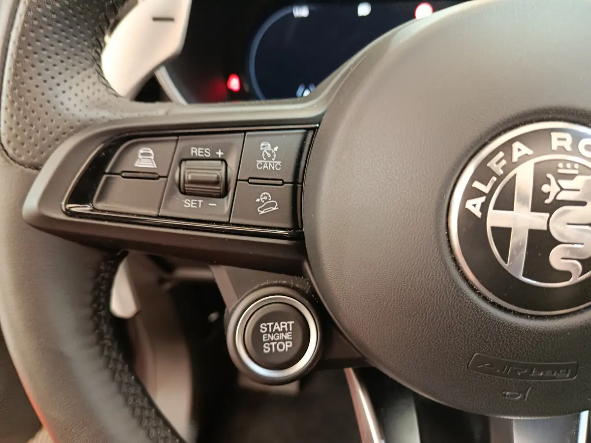 Gros plan sur le volant noir d'Alfa Romeo Stelvio avec boutons de régulateur et bouton démarrage Start Engine Stop.
