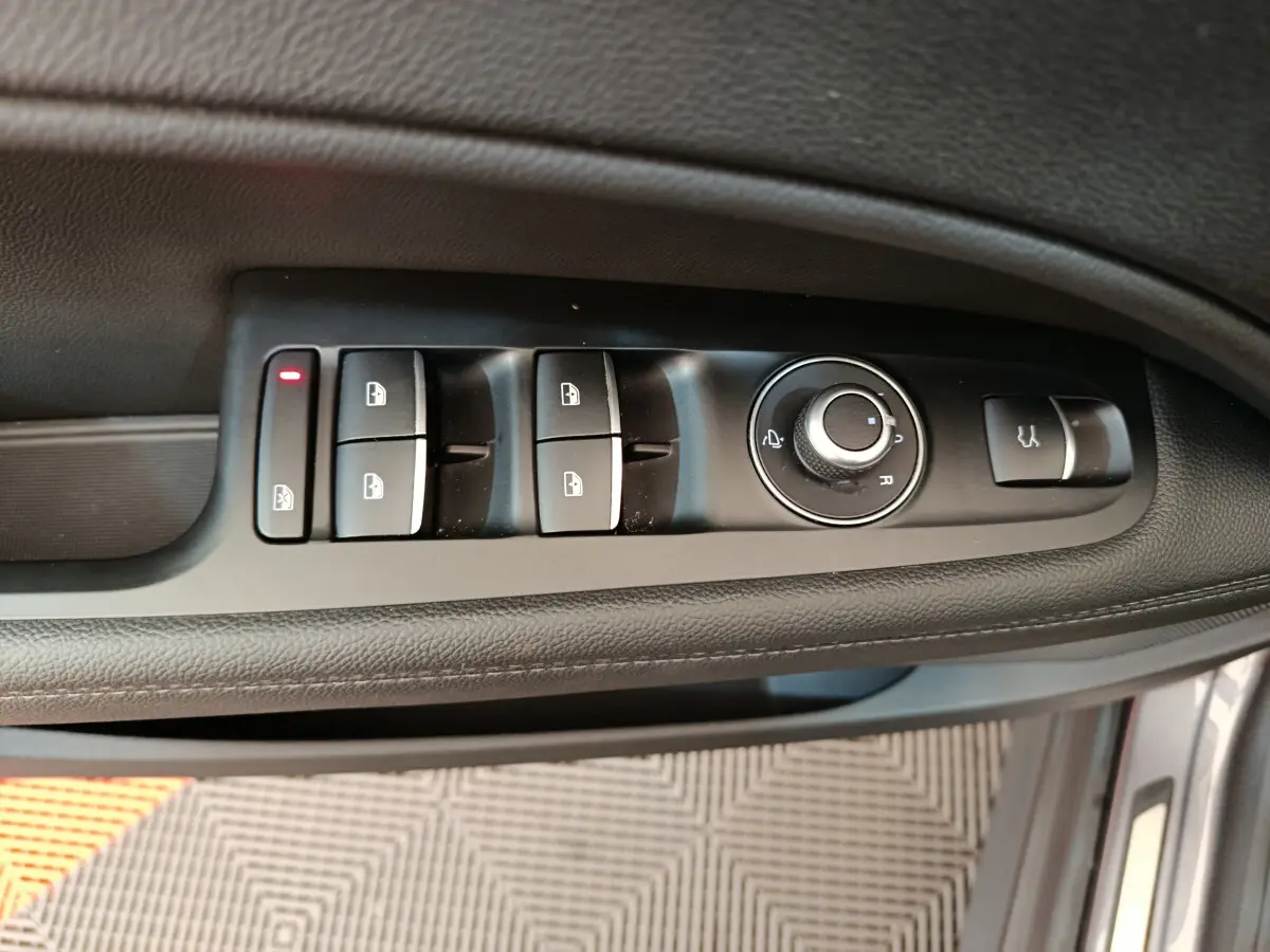 Vue rapprochée des commandes de lève-vitres et rétroviseurs sur la porte côté gauche d'un Alfa Romeo Stelvio gris foncé.