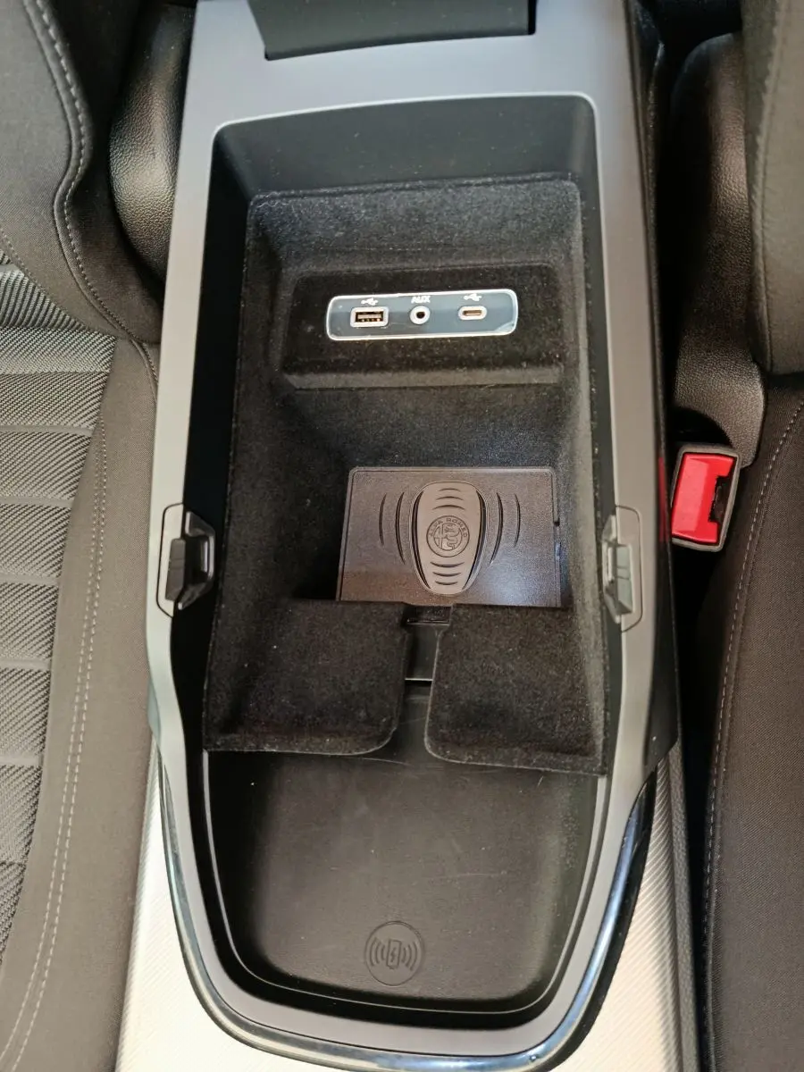 Vue plongeante sur la console centrale noire de l'Alfa Romeo Stelvio 2024 avec ports USB, prise AUX et zone de recharge sans fil.