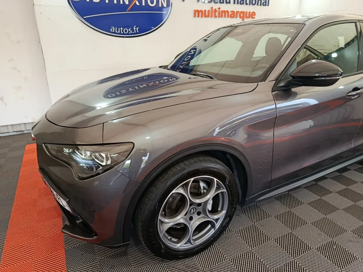 Vue 3/4 avant droit de l'Alfa Romeo Stelvio gris foncé avec jantes distinctives et phares LED ellipsoïdaux.