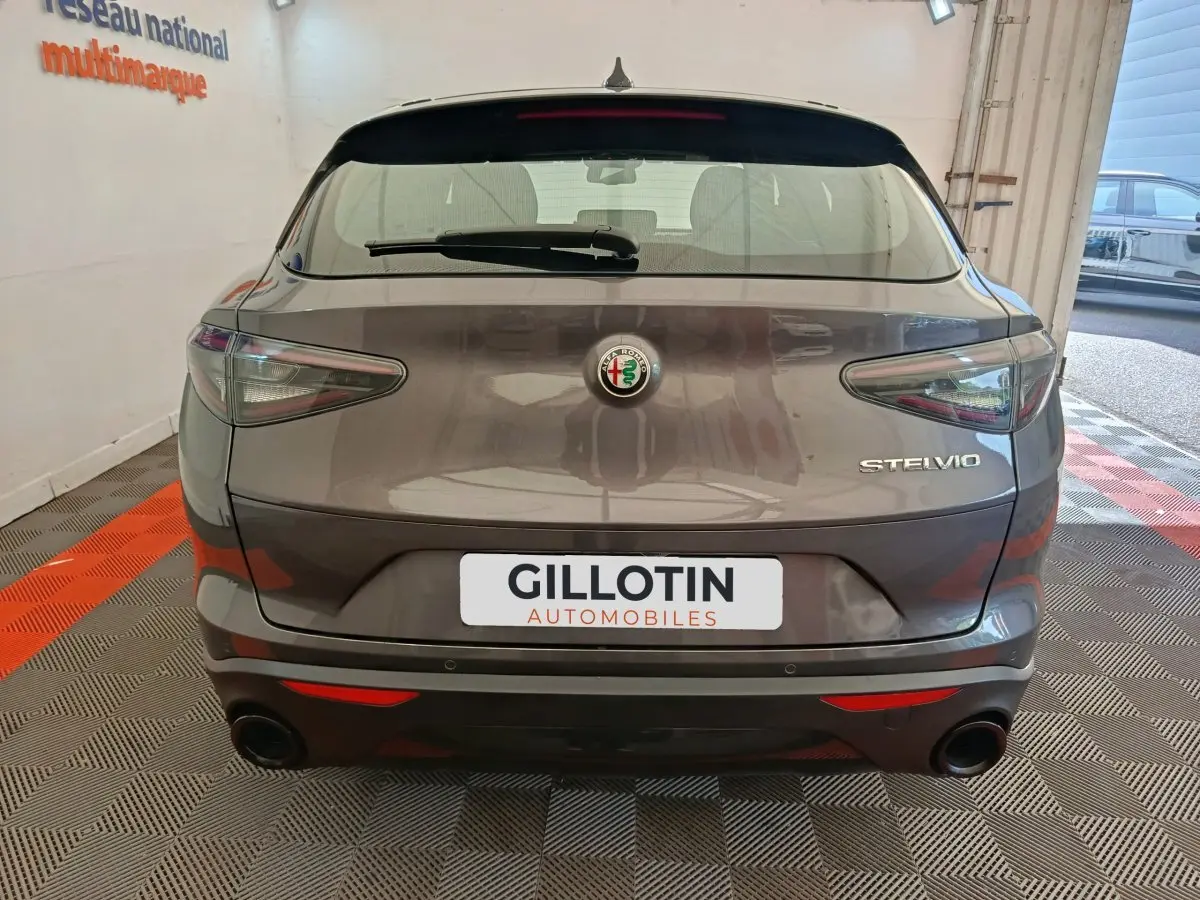 Vue arrière d'un Alfa Romeo Stelvio gris foncé avec feux effilés et double sortie d'échappement ronde.