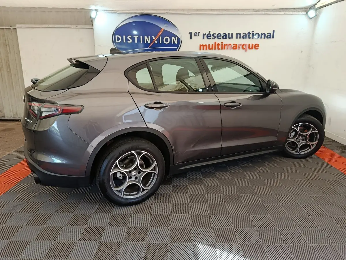 Vue de profil côté gauche d'un Alfa Romeo Stelvio gris foncé avec jantes distinctives en alliage, en intérieur showroom.