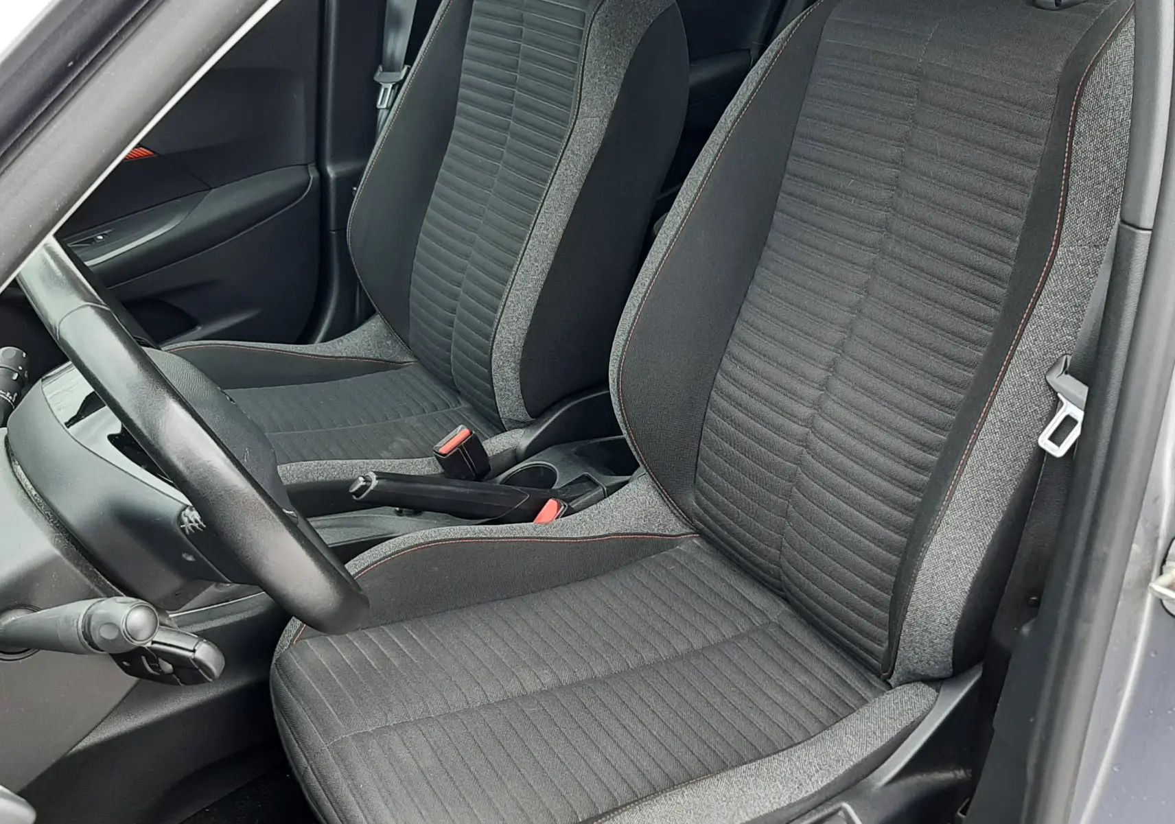 Vue intérieure côté conducteur du Peugeot 2008 2020, sièges tissu gris avec surpiqûres orange, volant et frein à main visibles.