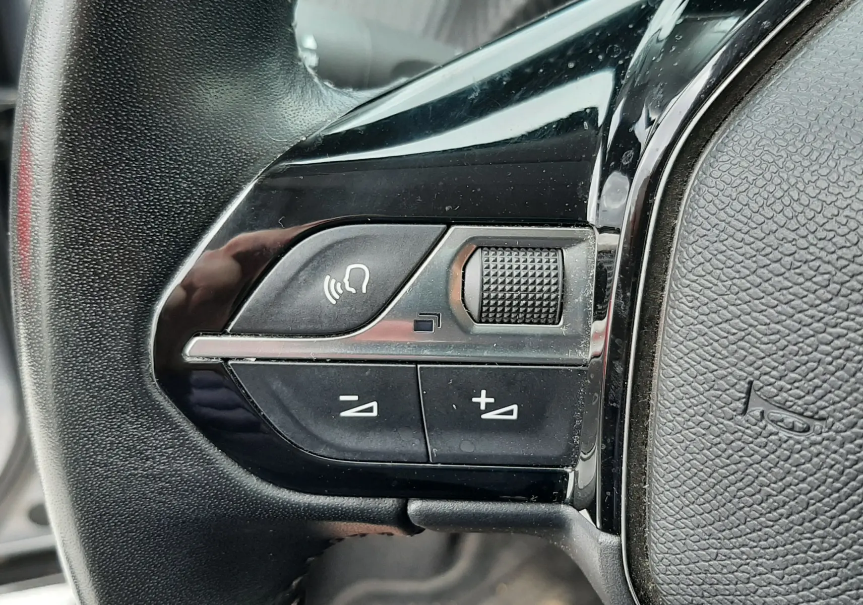 Gros plan sur les commandes gauche du volant noir du Peugeot 2008 gris Artense, avec boutons de volume et commande vocale.