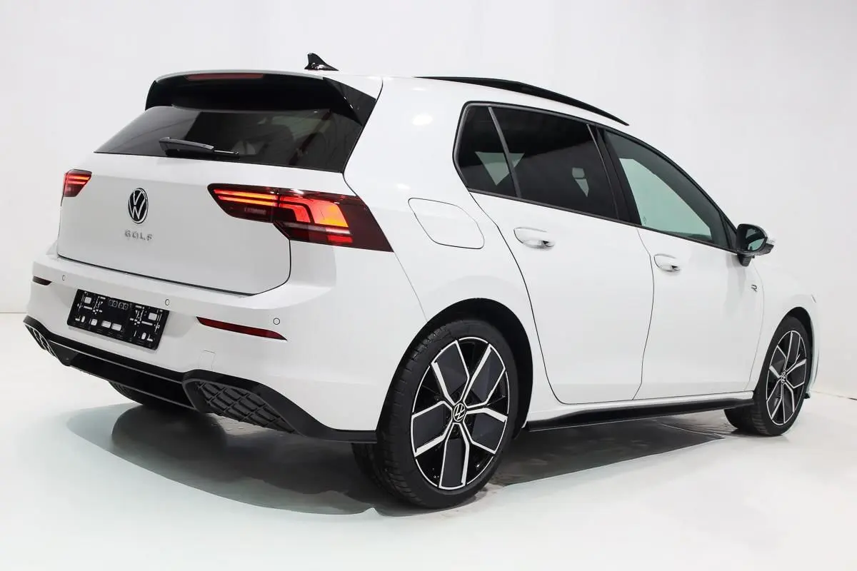 Vue 3/4 arrière droite d'une Volkswagen Golf blanche 2025 avec jantes alliage noires et toit panoramique noir.