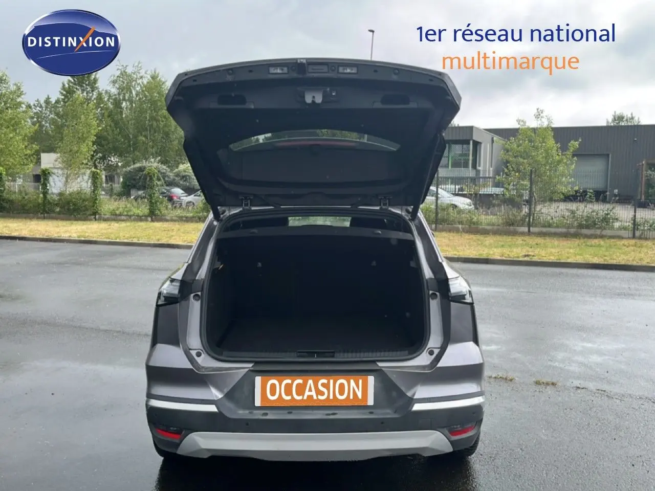 Vue arrière d'une Renault Symbioz gris cassiopée métal avec coffre ouvert sur un parking extérieur.