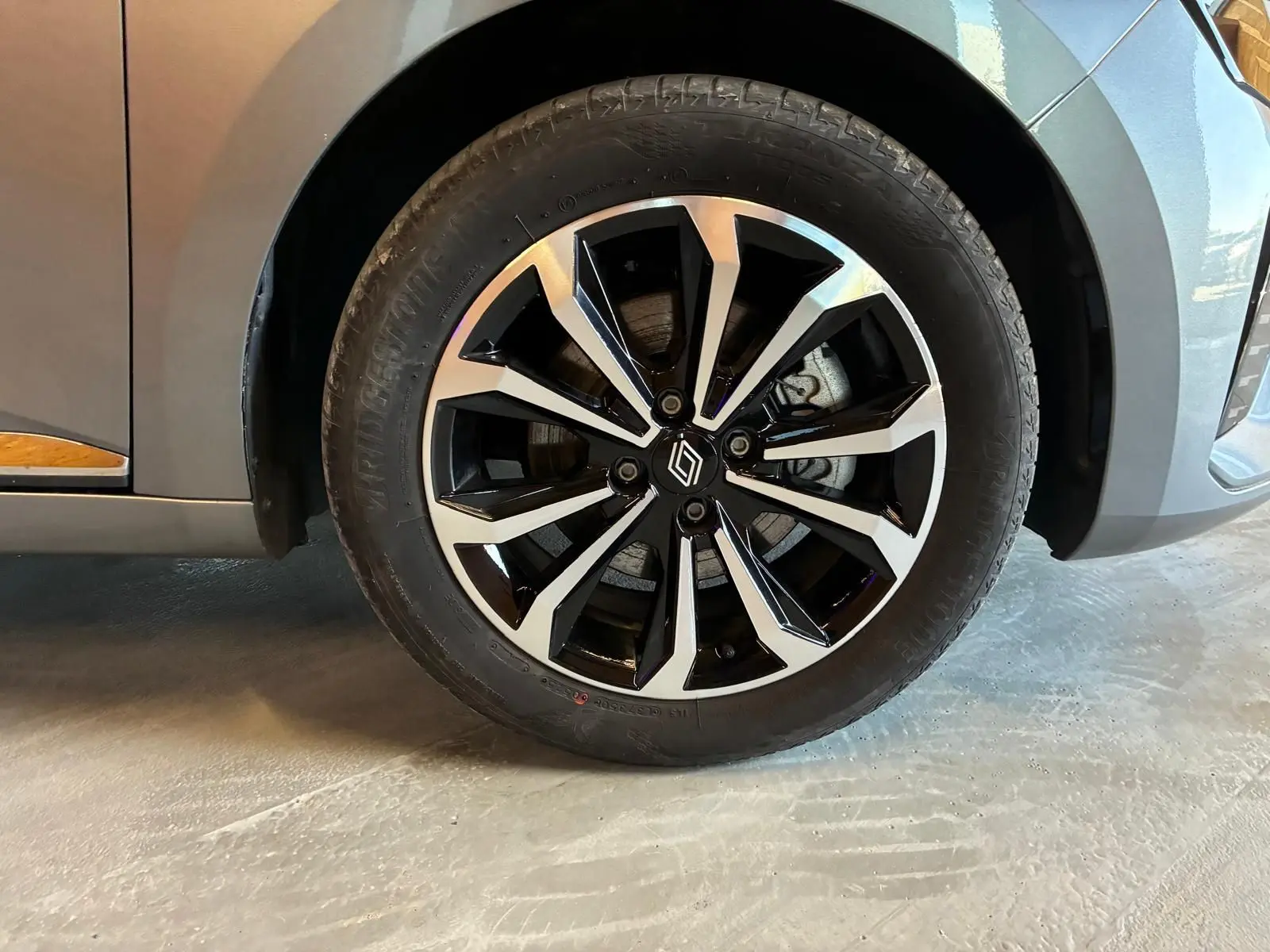 Gros plan sur la roue avant droite de la Renault Clio gris schiste, mettant en valeur la jante alliage bicolore au design moderne.