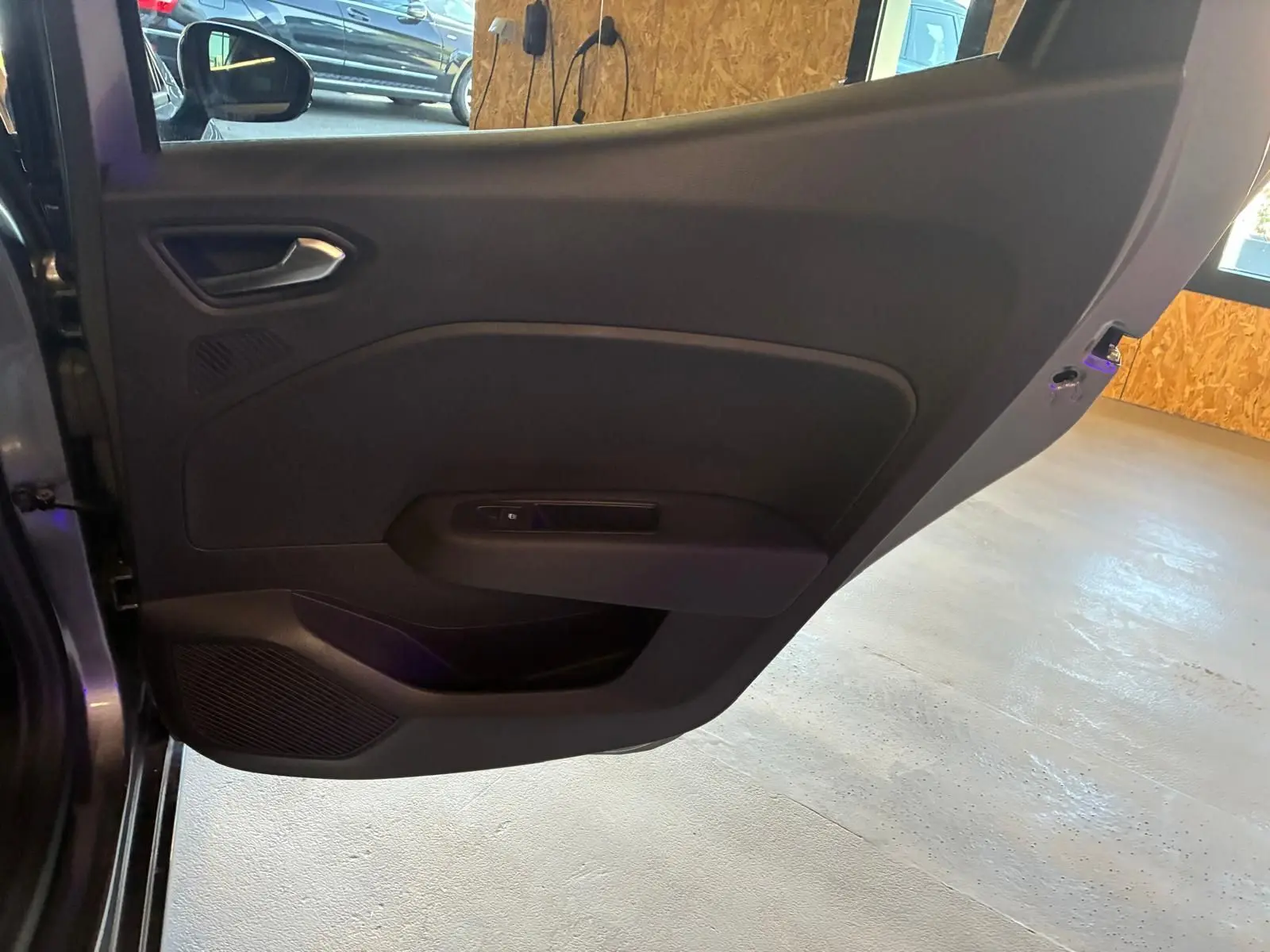 Détail de la porte arrière gauche ouverte d’une Renault Clio gris schiste, intérieur noir avec commande de vitre.