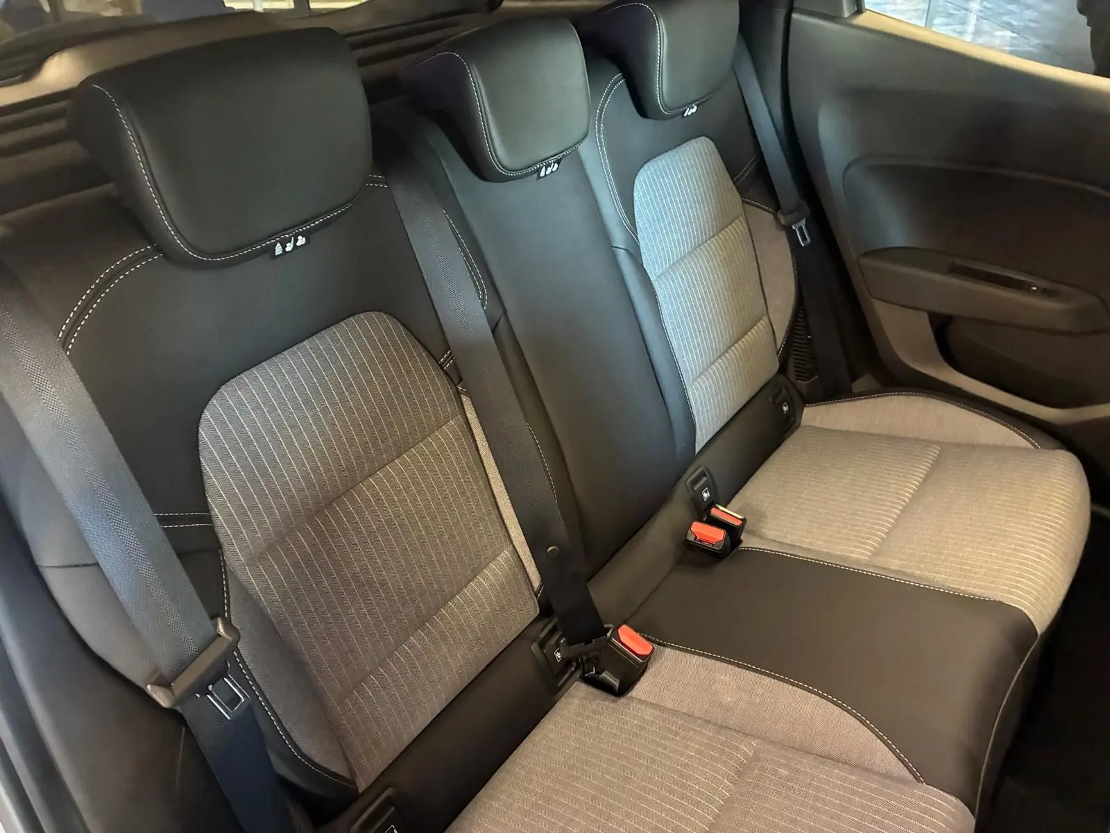 Vue intérieure sur les sièges arrière gris clair et noir de la Renault Clio hybride 2025, avec ceintures de sécurité visibles.