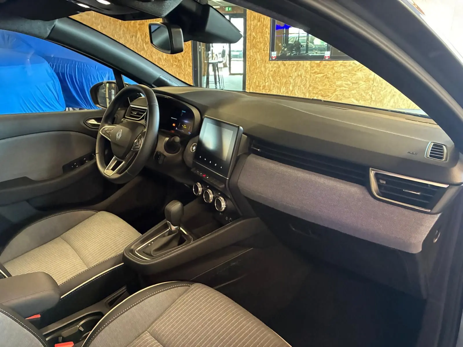 Vue intérieure côté conducteur de la Renault Clio 2025 gris schiste, avec tableau de bord moderne et écran tactile central.