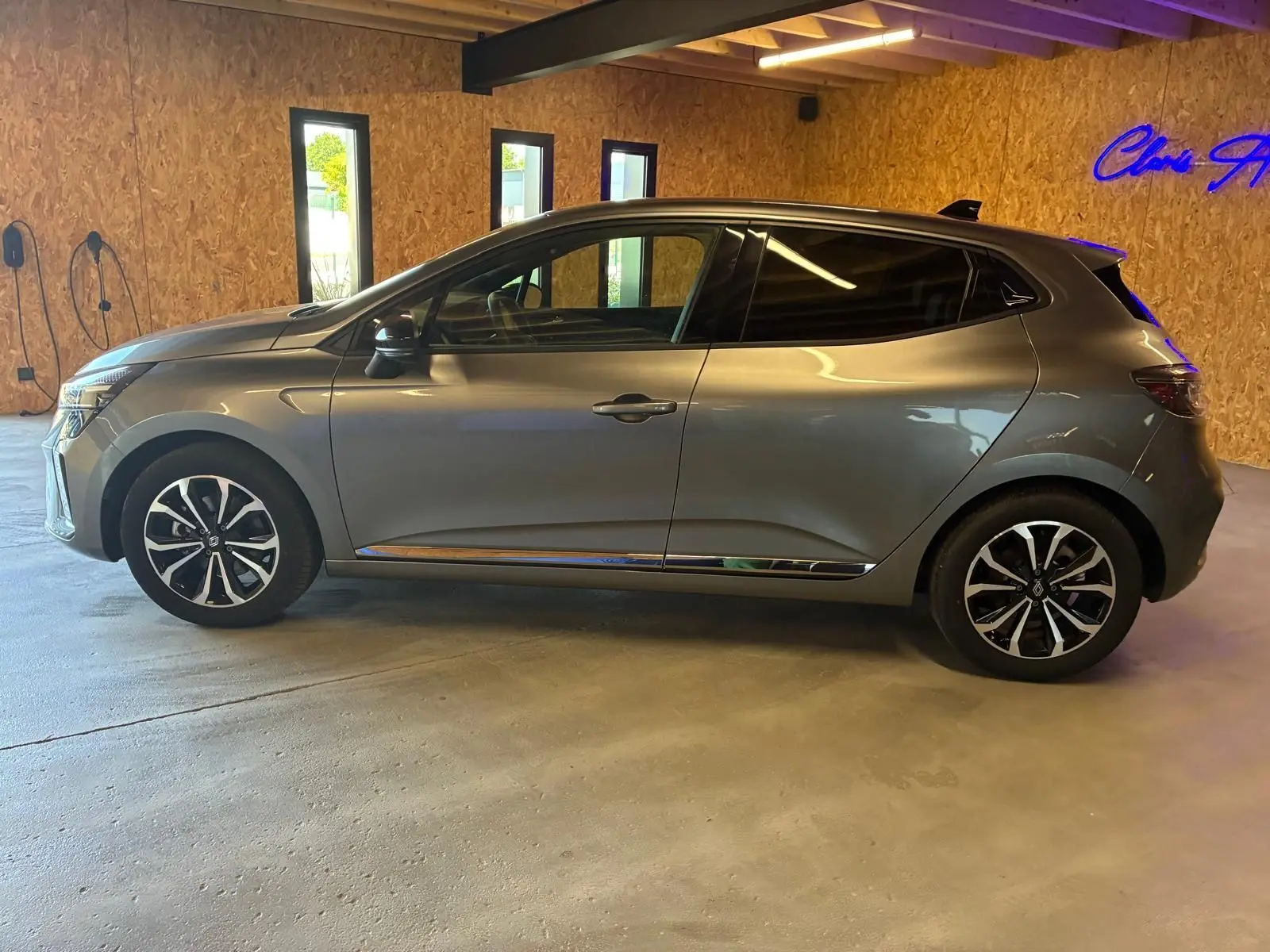 Profil droit d'une Renault Clio 2025 gris schiste, avec jantes alliage et vitres teintées, stationnée en intérieur.