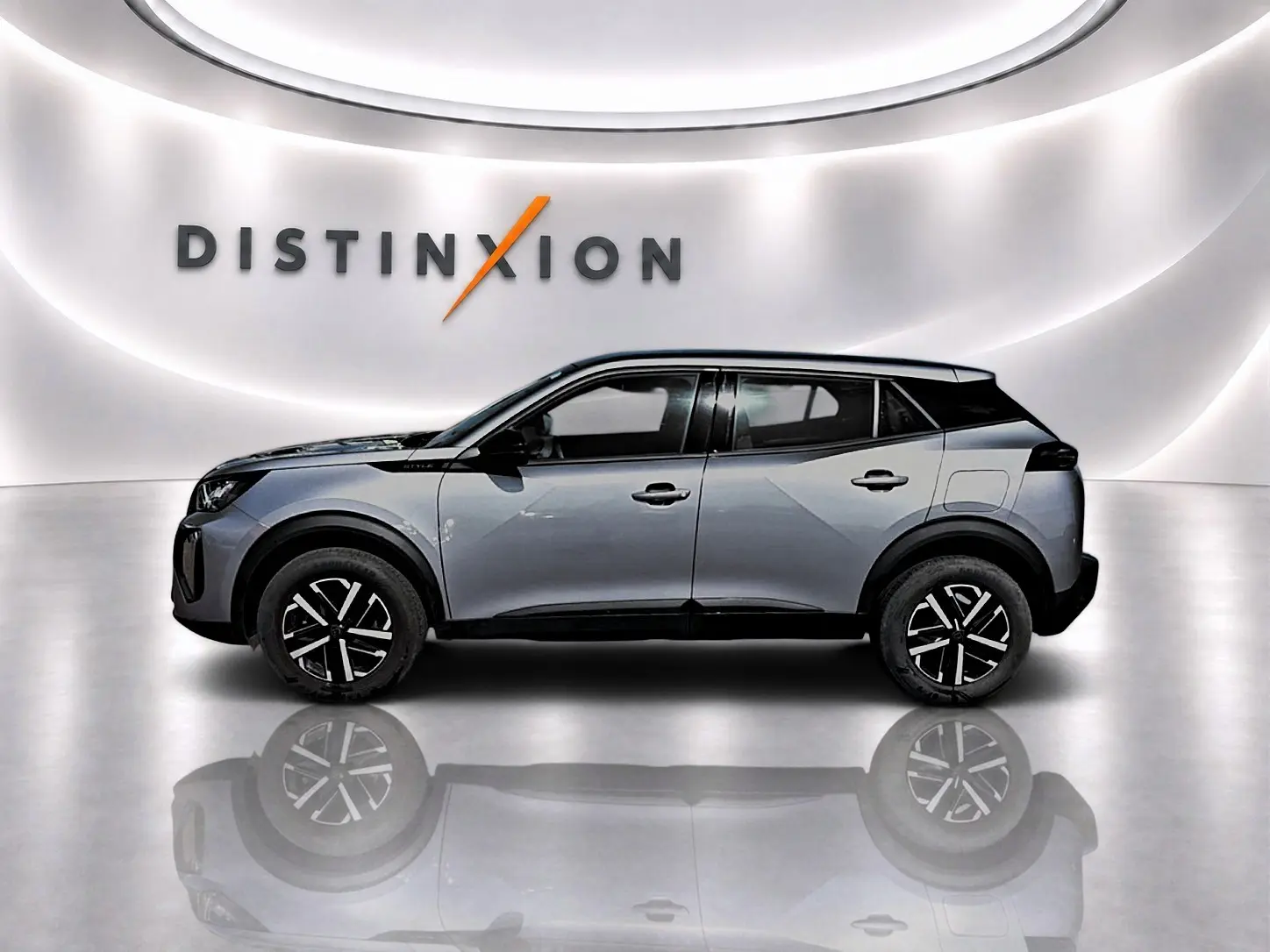 Profil côté gauche d’un Peugeot 2008 gris 2025 avec toit noir et jantes à motif bicolore dans un showroom lumineux.