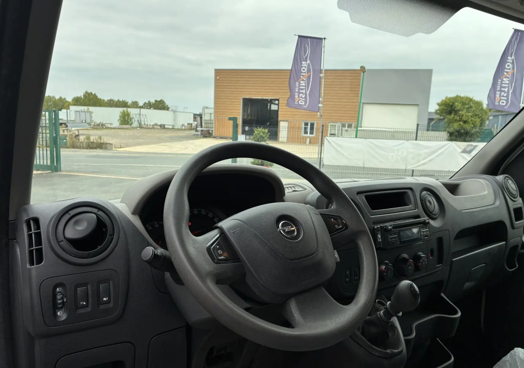 Vue intérieure du tableau de bord et volant noir d'un Opel Movano Fourgon blanc, version 2017, côté conducteur.