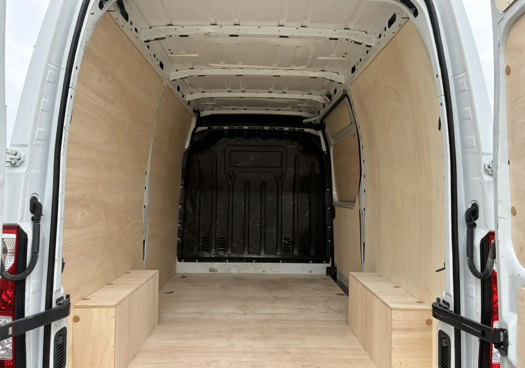 Intérieur du fourgon Opel Movano blanc 2017 vu de l'arrière, avec aménagement bois clair sur les parois et le sol.