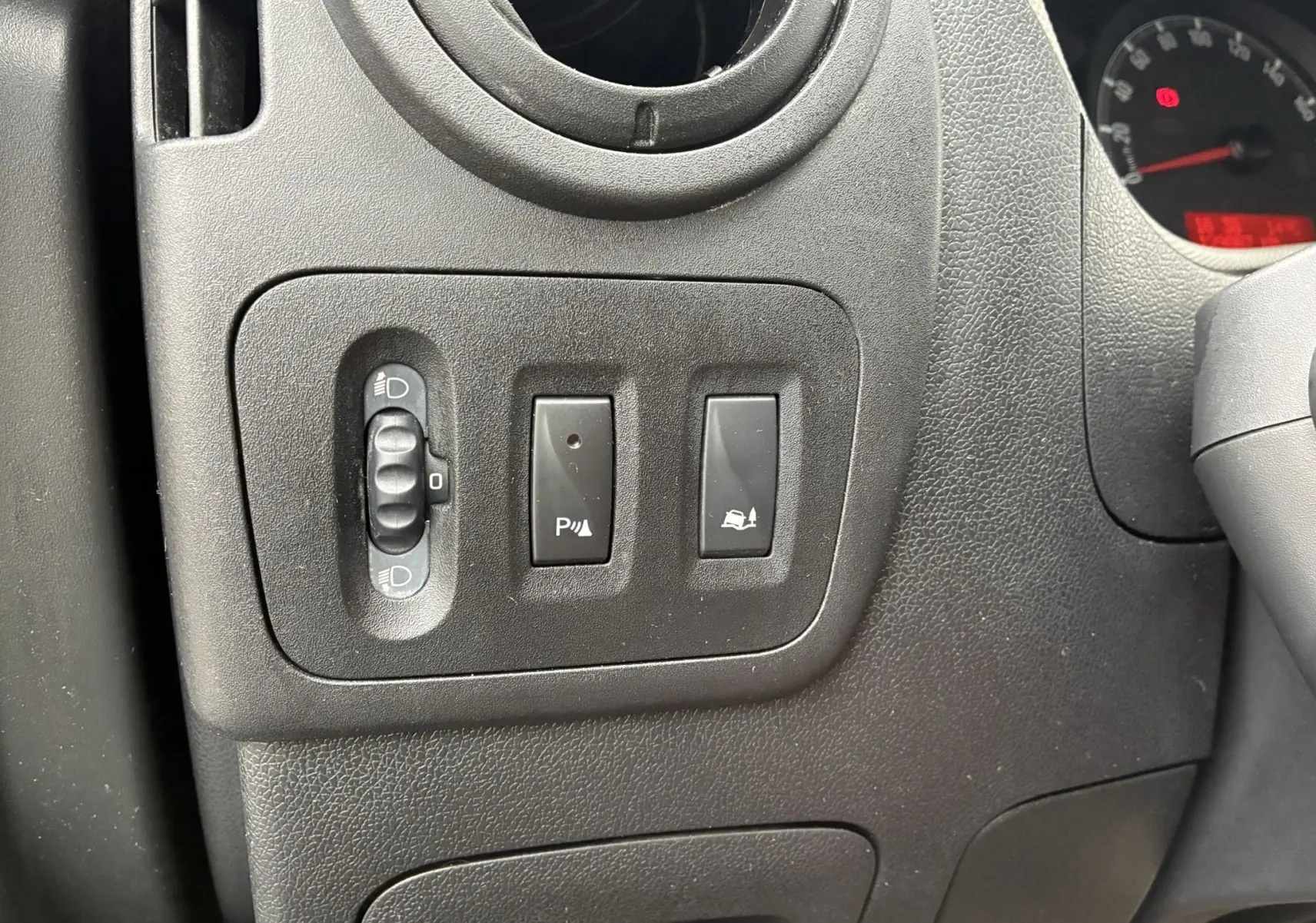 Gros plan sur les commandes de réglage des phares et d'assistance au stationnement du tableau de bord noir d'un Opel Movano Fourgon blanc.