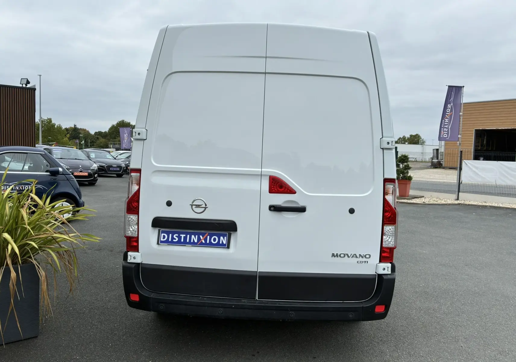 Vue arrière d'un fourgon Opel Movano blanc avec portes battantes et logo distinctif sur parking.