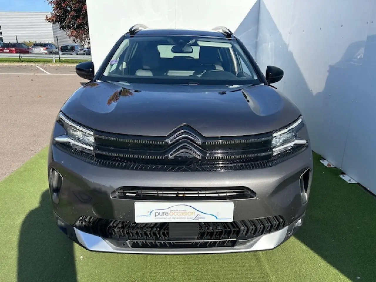 Citroën C5 Aircross gris platinium vue de face, avec calandre noire et barres de toit visibles sur fond extérieur.