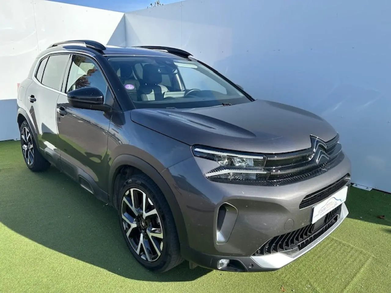 Citroën C5 Aircross gris platinium en 3/4 avant droit, avec barres de toit et jantes alliage noires.