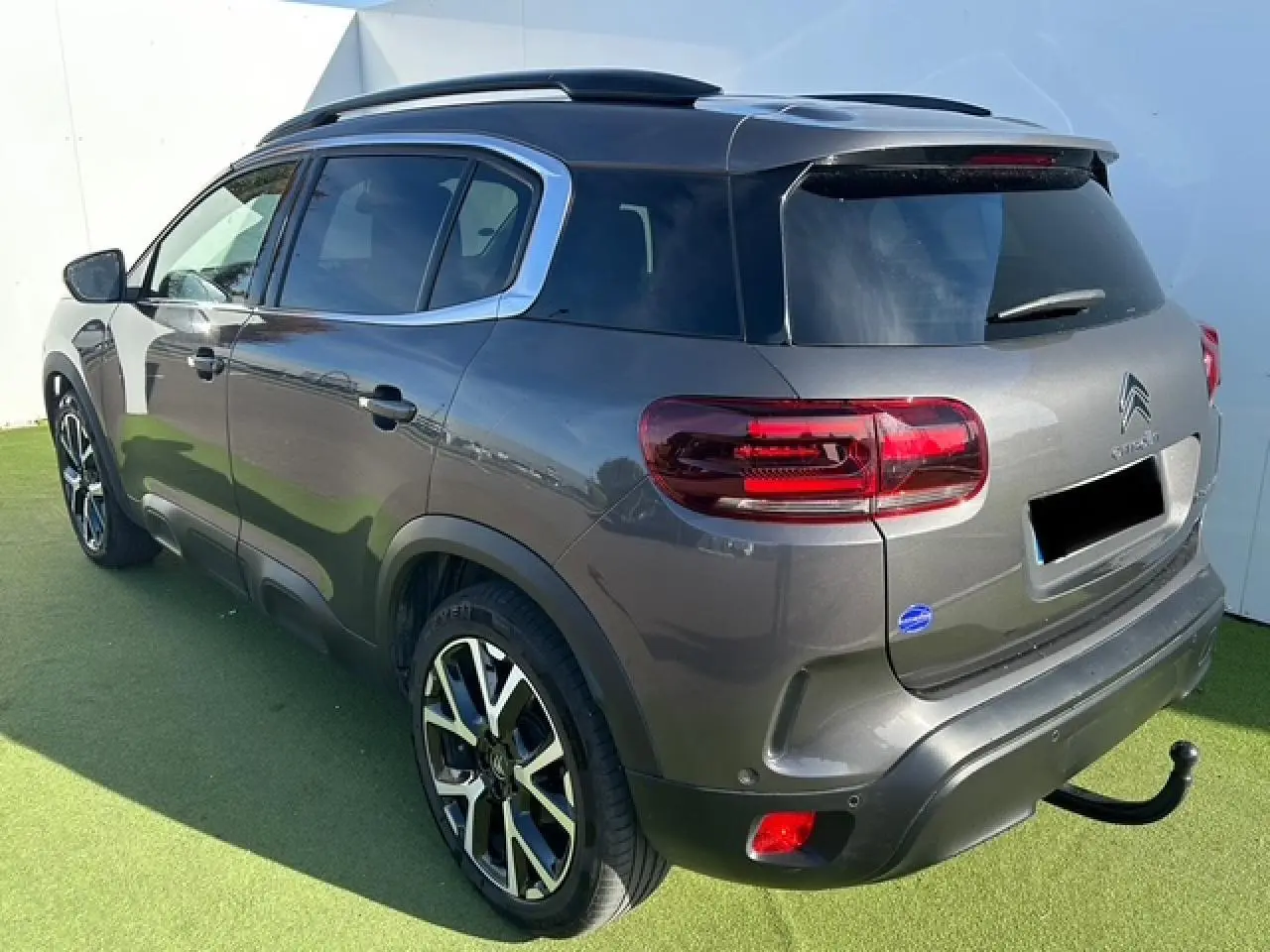 Vue 3/4 arrière droit du Citroën C5 Aircross gris platinium avec barres de toit et attelage visible.