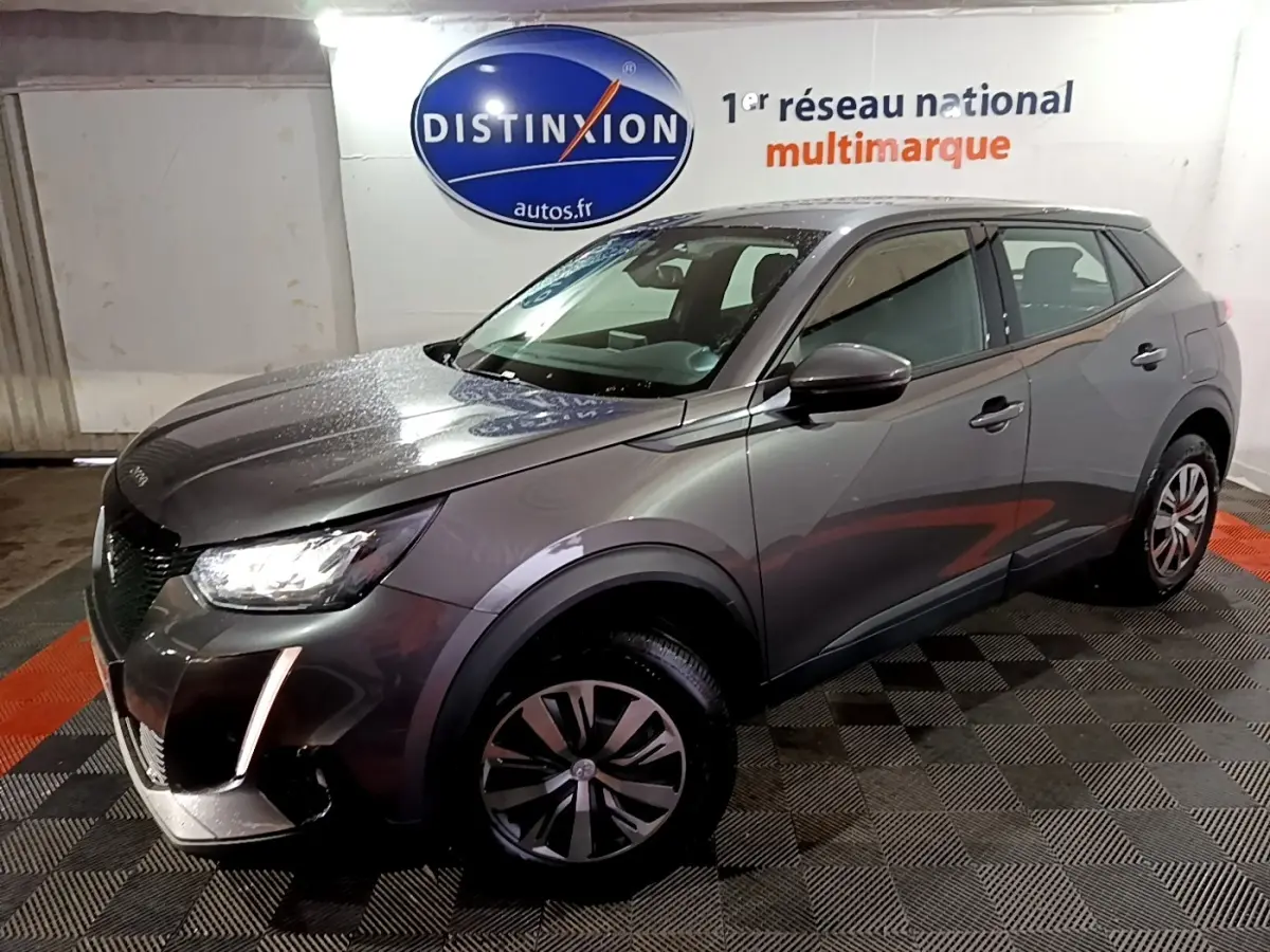 Peugeot 2008 gris clair vue 3/4 avant droit, avec phares LED et jantes alliage distinctives, en intérieur showroom.