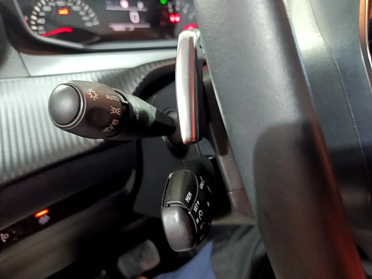 Gros plan sur le volant cuir et les commandes au volant du Peugeot 2008 gris clair, tableau de bord en arrière-plan.