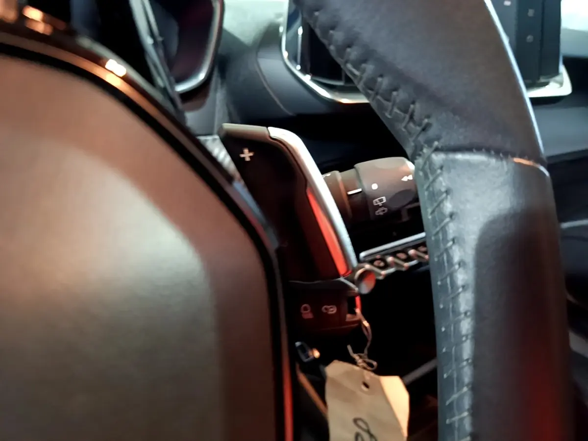 Gros plan sur le volant cuir noir et la palette de changement de vitesse à droite du Peugeot 2008 gris clair, intérieur moderne.