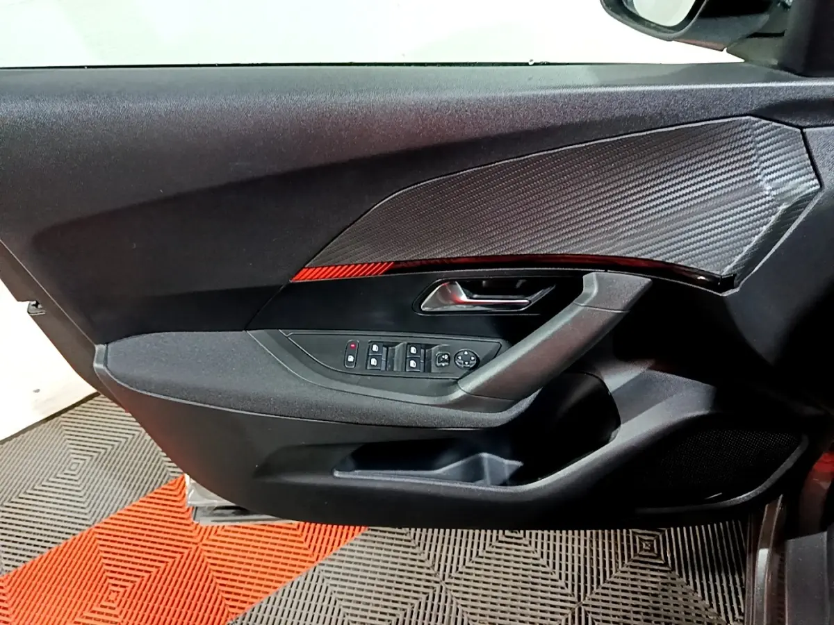 Vue intérieure côté gauche de la porte avant d’un Peugeot 2008 gris clair, avec commandes électriques et insert décoratif noir.