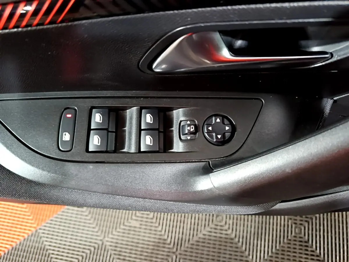 Gros plan sur les commandes des vitres et rétroviseurs sur la porte côté gauche d’un Peugeot 2008 gris clair.