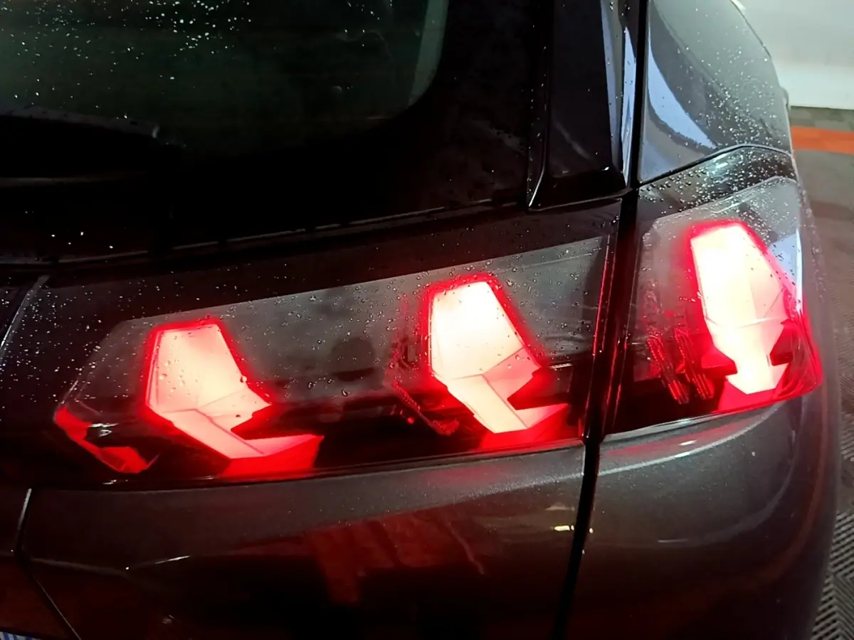 Gros plan sur les feux arrière allumés d'une Peugeot 2008 gris clair, vue côté droit sous la pluie.
