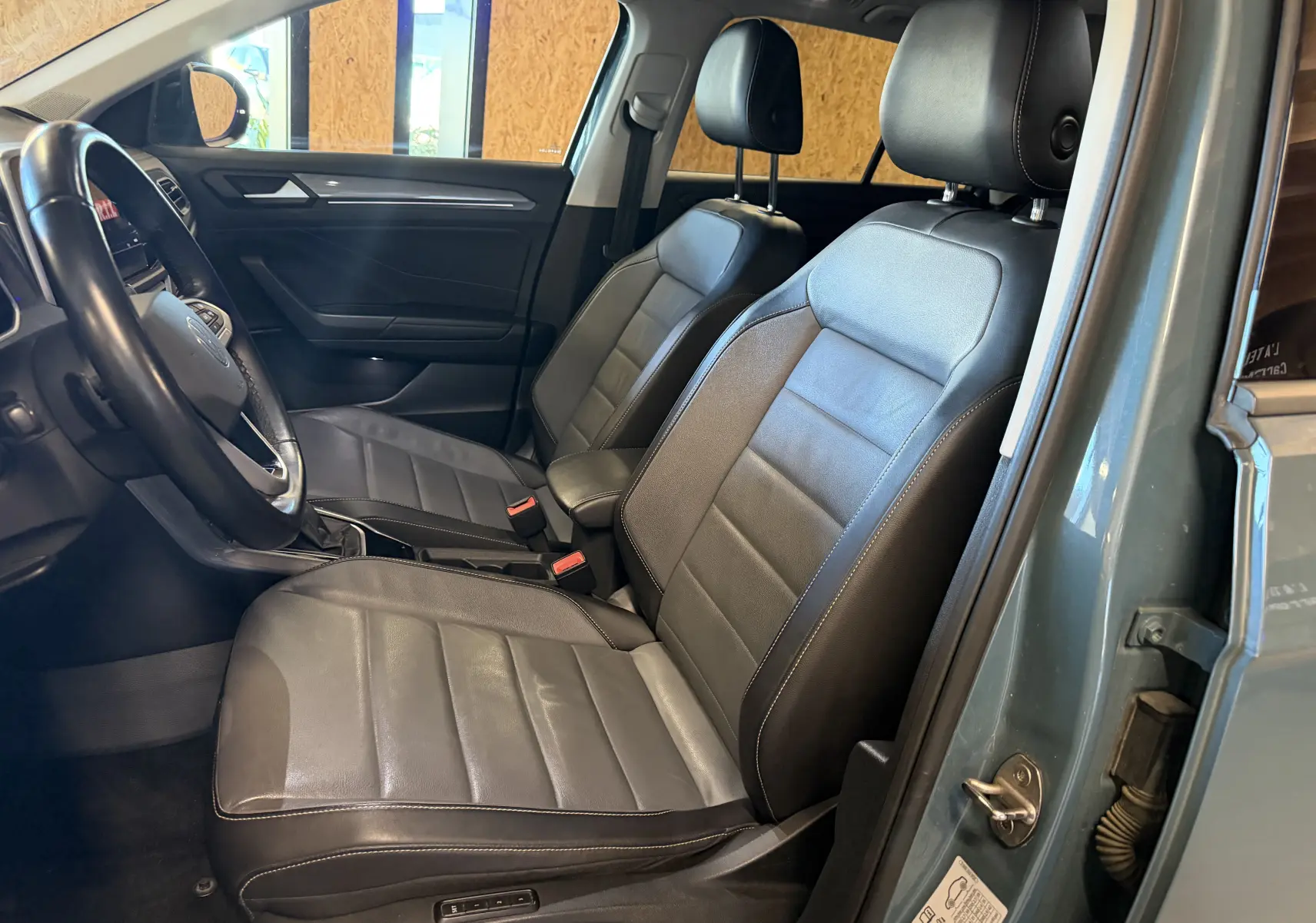 Vue intérieure côté conducteur du Volkswagen T-Roc bleu 2022, mettant en valeur les sièges cuir noir et le volant.