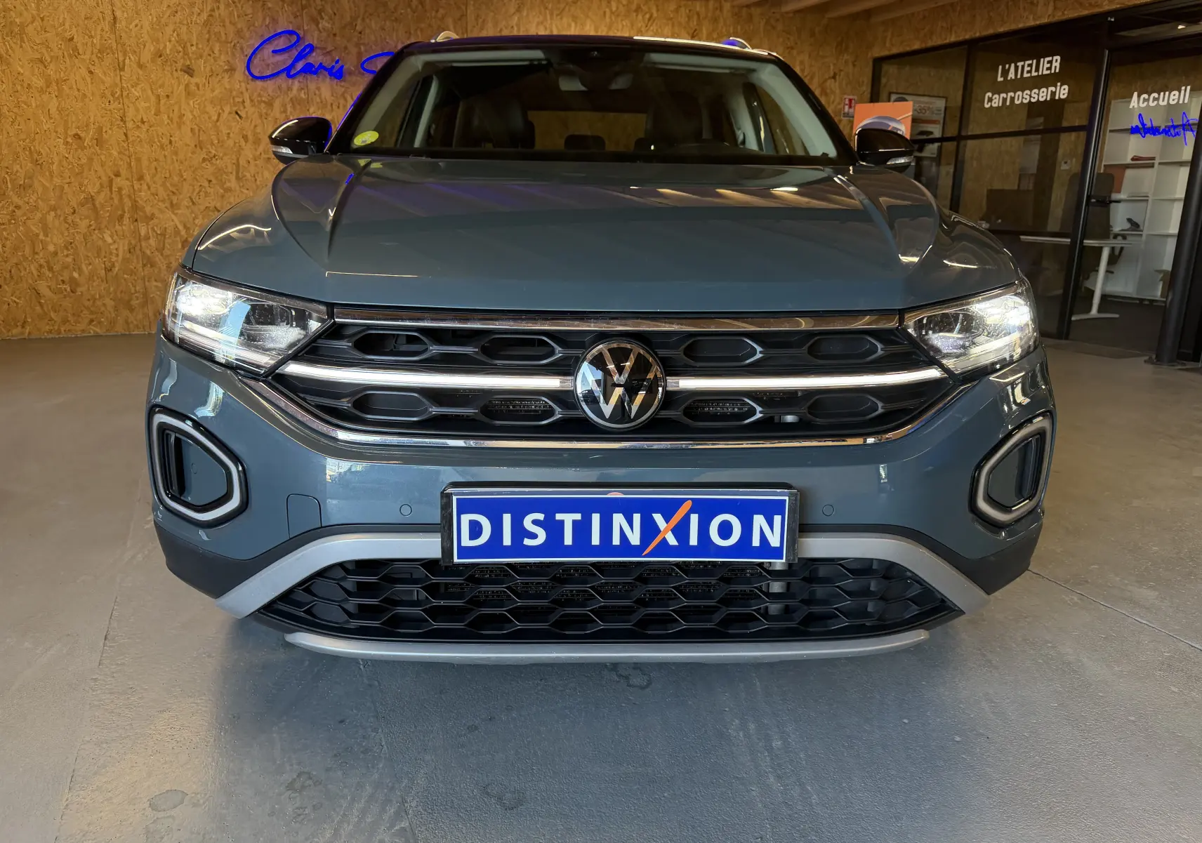 Volkswagen T-Roc bleu en 3/4 avant droit dans un intérieur avec éclairage naturel, calandre et phares LED visibles.