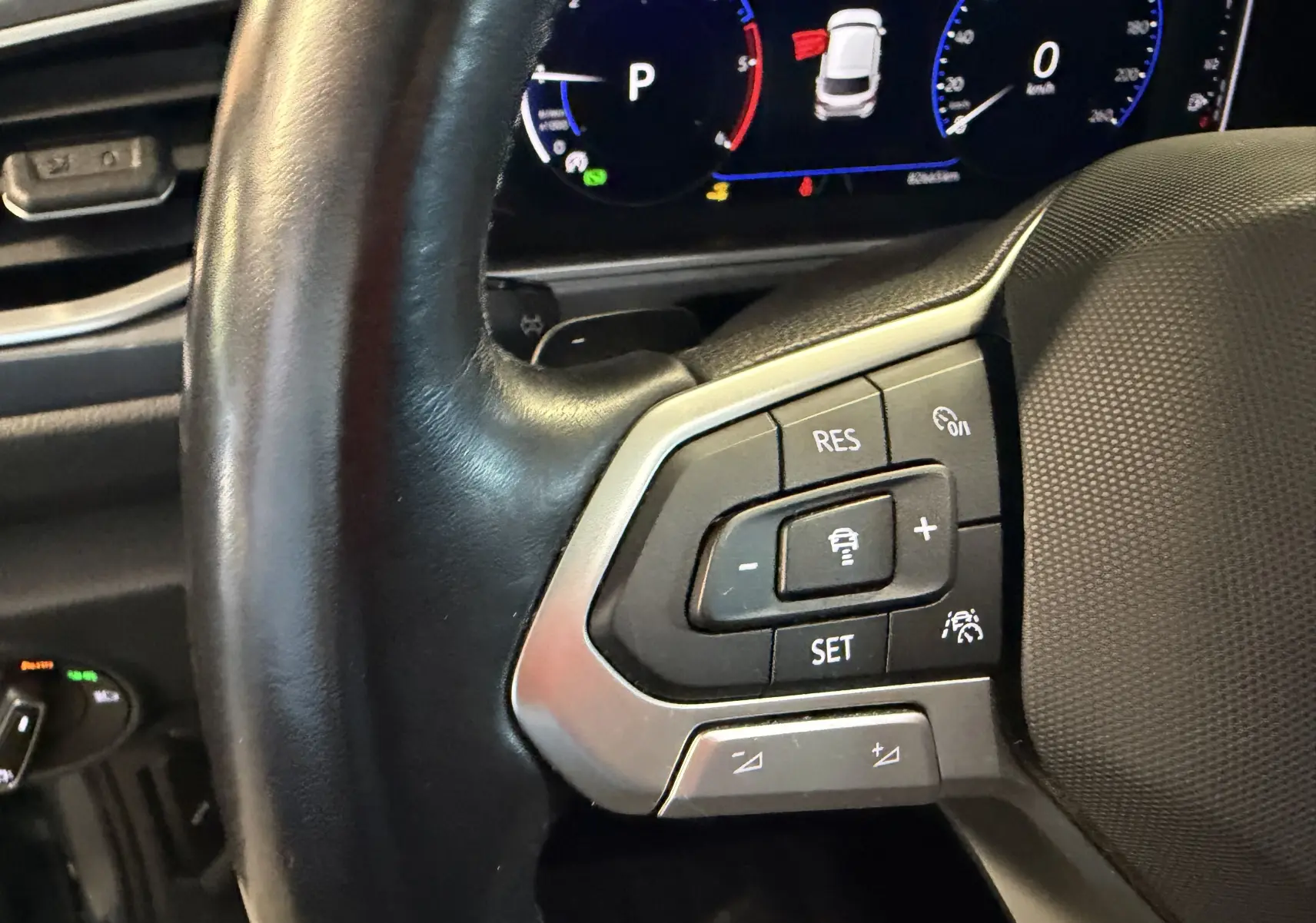 Gros plan sur le volant noir du Volkswagen T-Roc 2022, mettant en valeur les commandes de régulateur de vitesse et l'écran digital en arrière-plan.