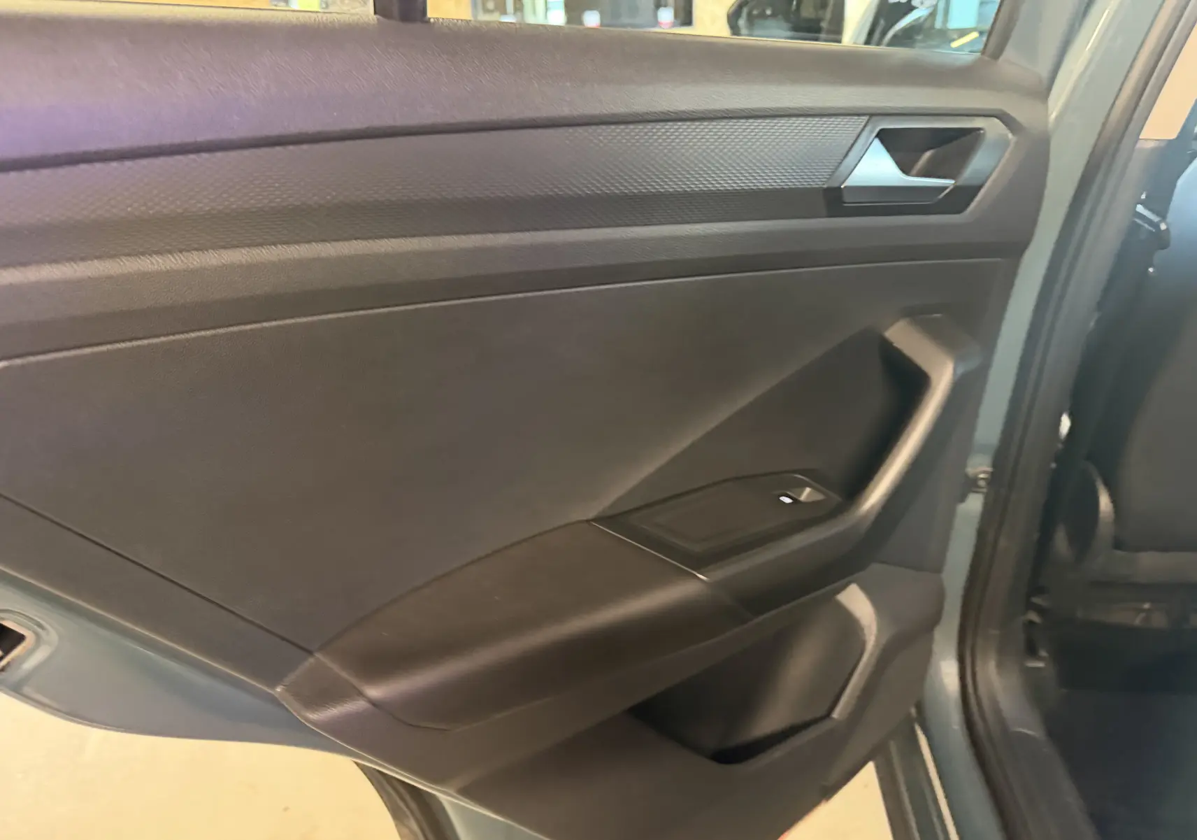 Vue intérieure du panneau de porte arrière gauche du Volkswagen T-Roc bleu 2022, avec commande de fenêtre visible.