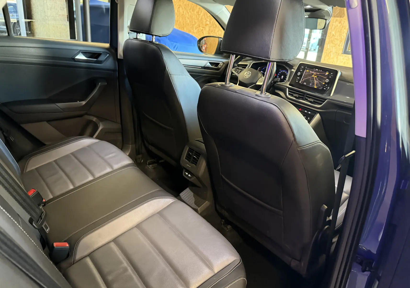 Vue intérieure arrière du Volkswagen T-Roc bleu 2022, mettant en valeur les sièges en cuir noir et la console centrale avec écran tactile.