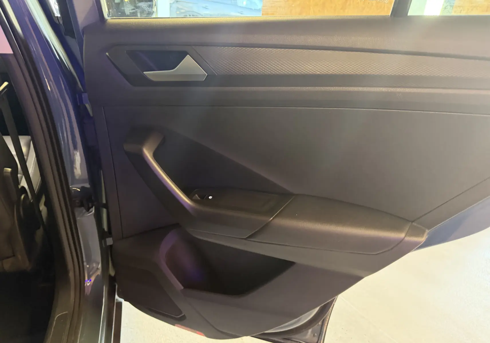 Vue intérieure de la porte arrière gauche du Volkswagen T-Roc bleu 2022, avec garniture noire et poignée intégrée.