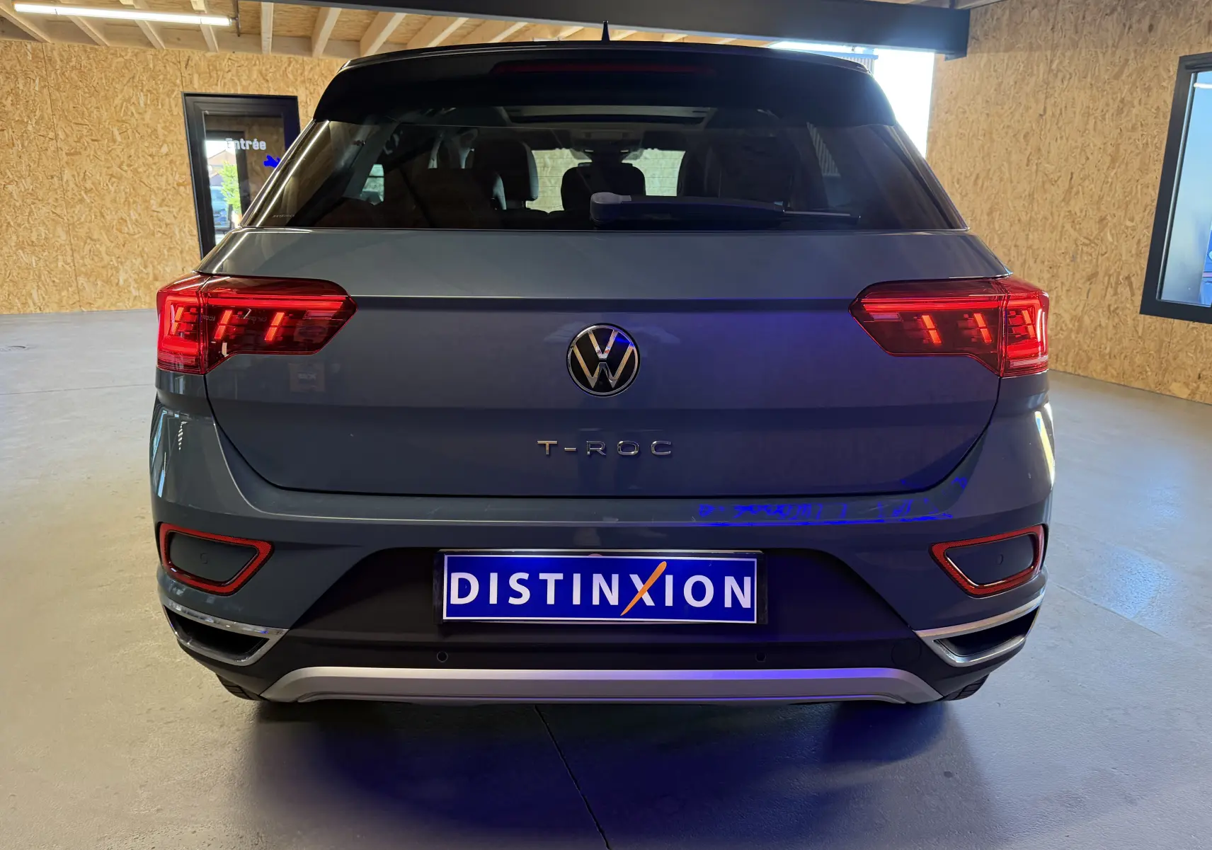 Vue arrière d'un Volkswagen T-Roc bleu 2022 avec feux allumés et plaque Distinxion dans un garage.