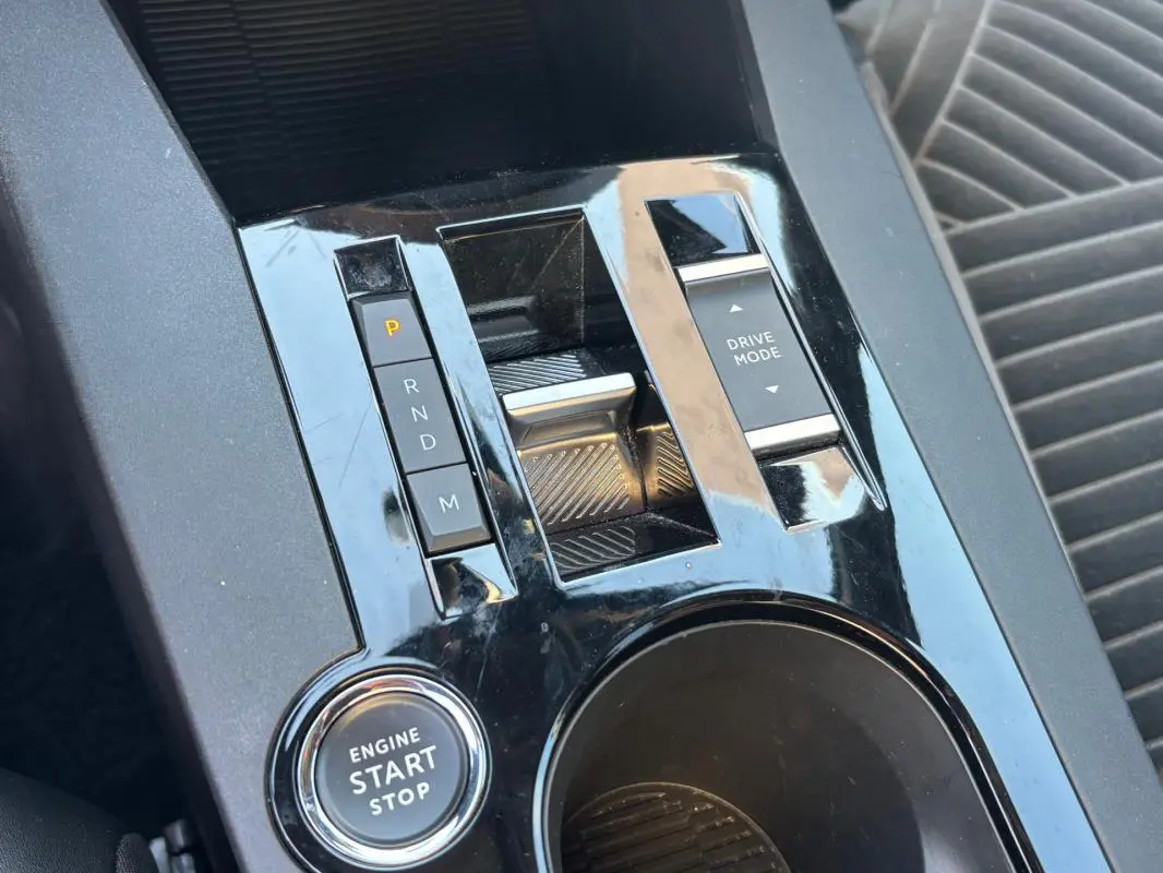 Gros plan sur la console centrale noire brillante de la Lancia Ypsilon 1.2 Ibrida avec bouton start/stop et commandes boîte auto.