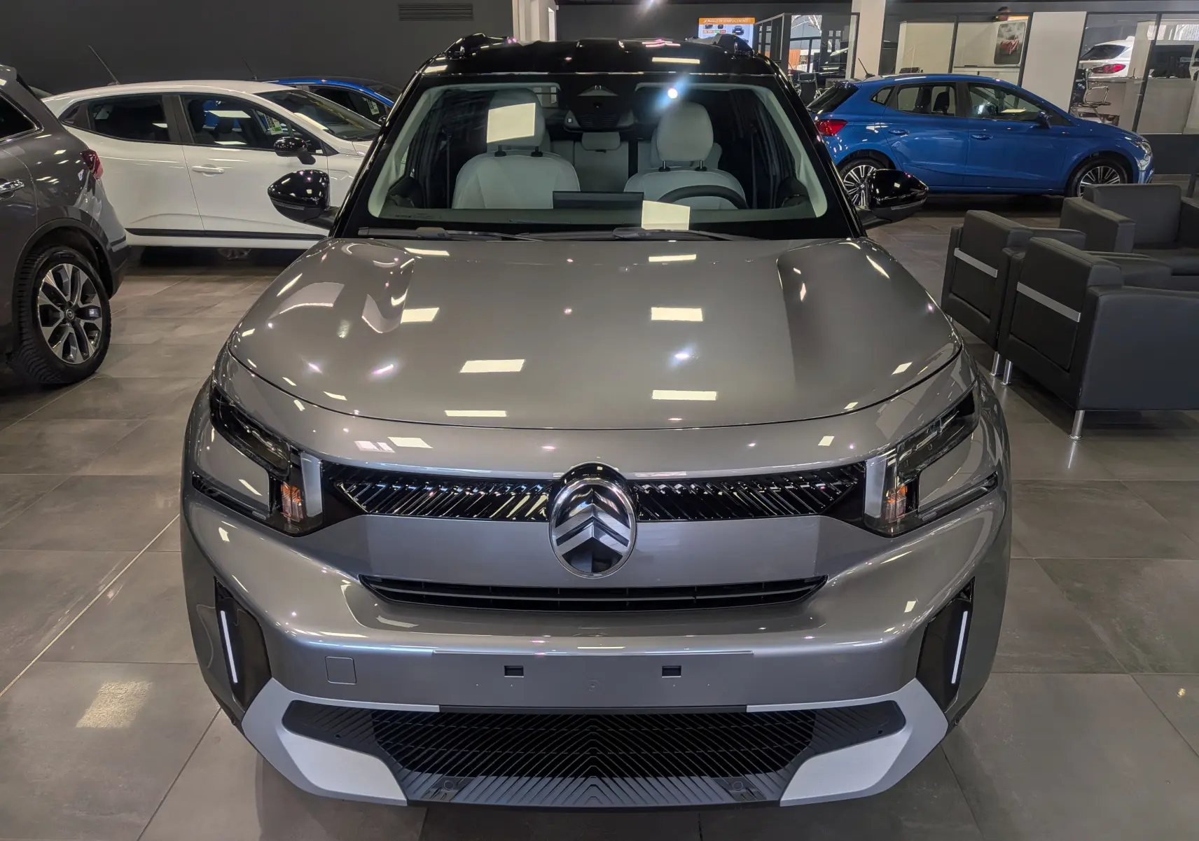 Vue frontale d'un Citroën C3 Aircross 2026 hybride gris Mercury avec toit noir en showroom.