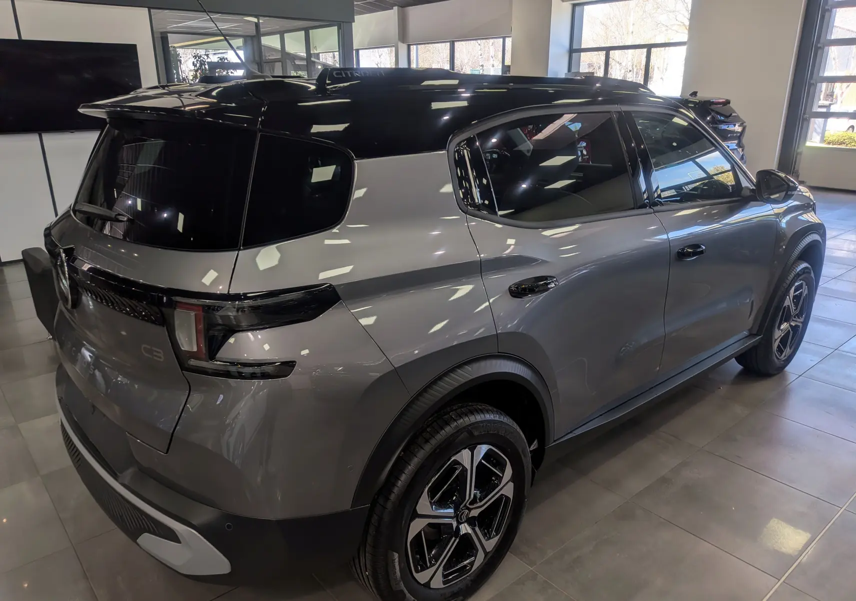 Vue 3/4 arrière droite du Citroën C3 Aircross hybride gris Mercury avec toit noir et jantes bi-ton en showroom.
