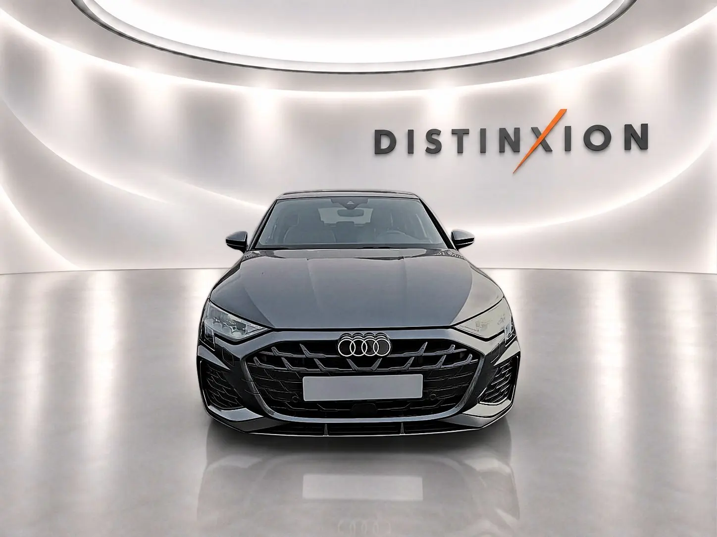 Audi A3 Sportback gris Daytona vue de face dans un showroom avec éclairage moderne et logo Distinxion en arrière-plan.