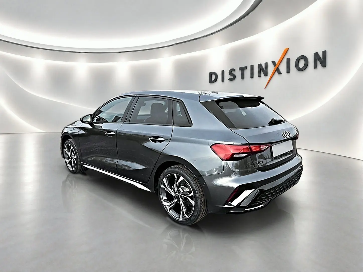 Audi A3 Sportback gris Daytona vue 3/4 arrière droit dans un showroom lumineux avec jantes alu distinctives.