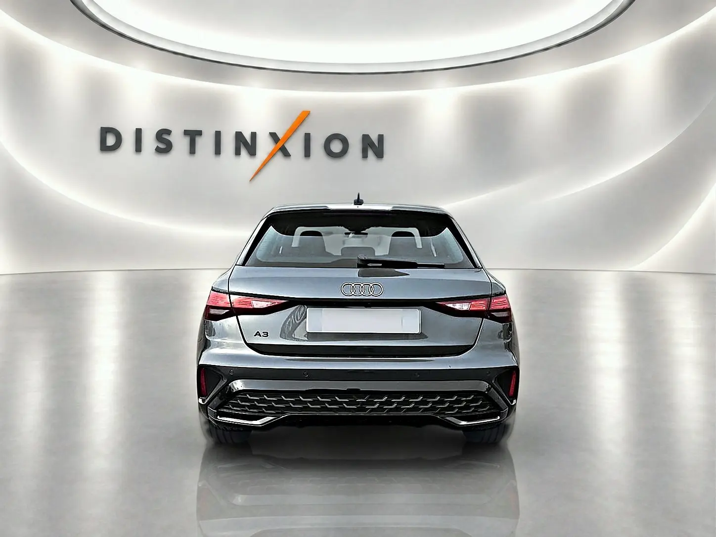 Vue arrière d'une Audi A3 Sportback gris Daytona dans un showroom lumineux avec logo Distinxion en arrière-plan.