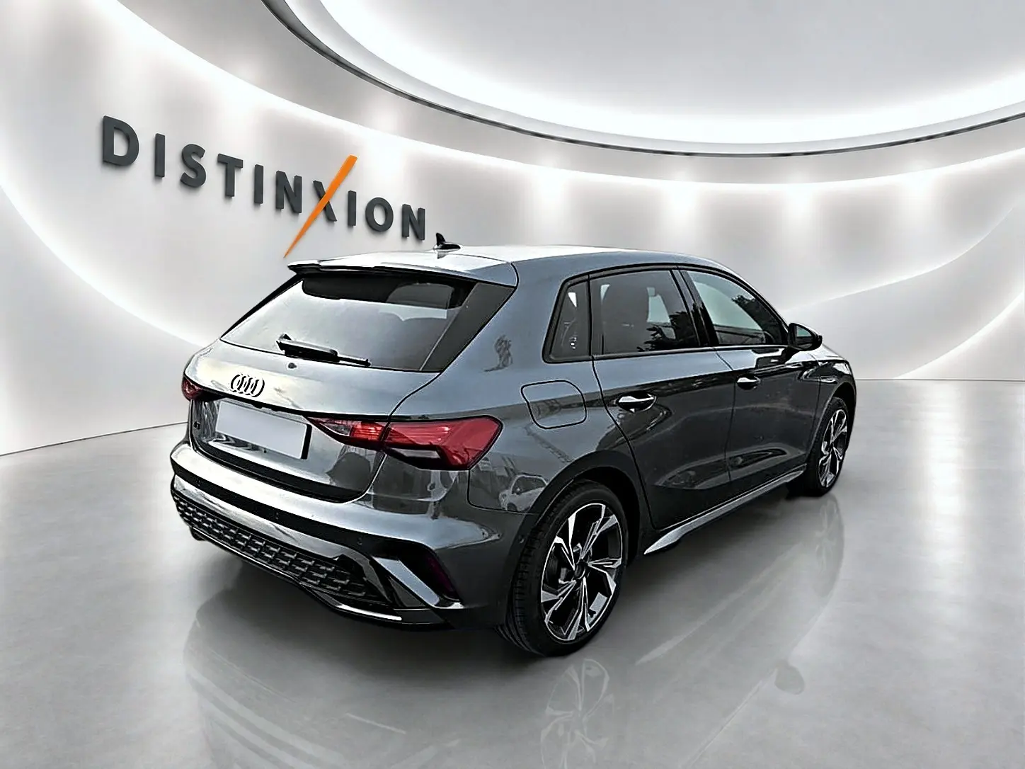 Audi A3 Sportback gris Daytona vue 3/4 arrière droit dans un showroom lumineux avec jantes alu distinctives.