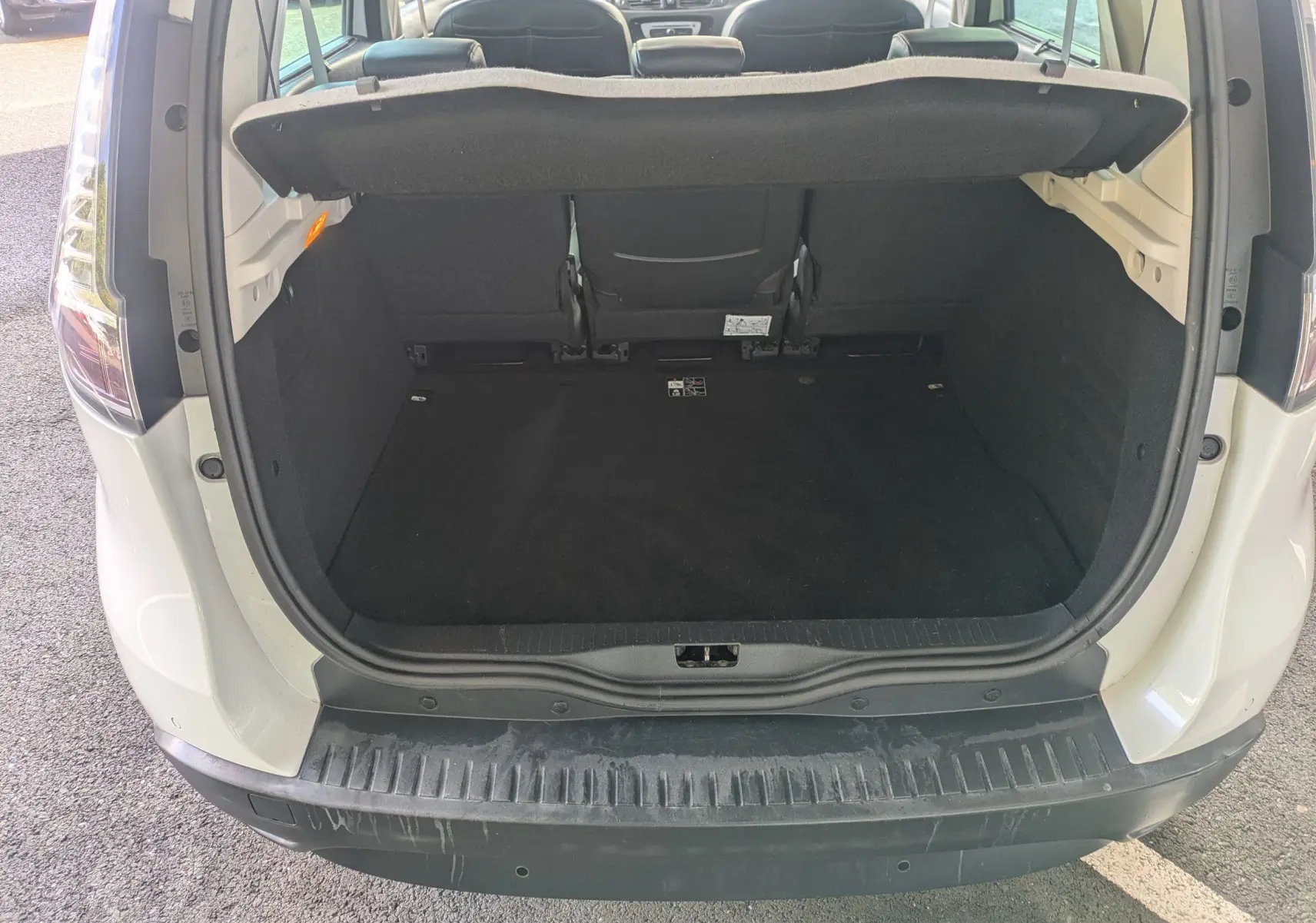 Coffre ouvert vu de l'arrière d'un Renault Scenic IV blanc, montrant l'espace de chargement et la banquette arrière.
