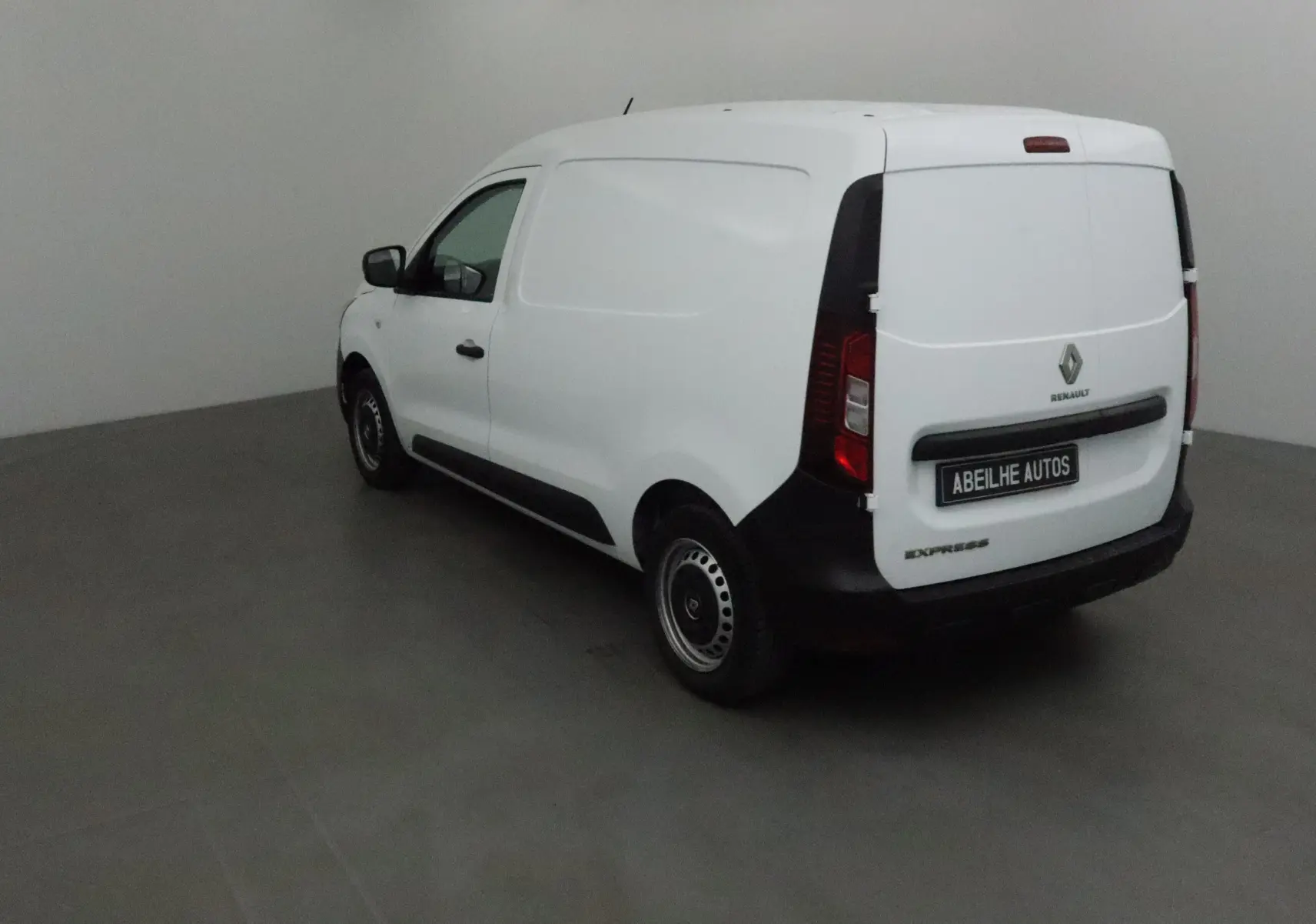 Renault Express Van blanc vu en 3/4 arrière droit dans un espace intérieur neutre sans fenêtres.