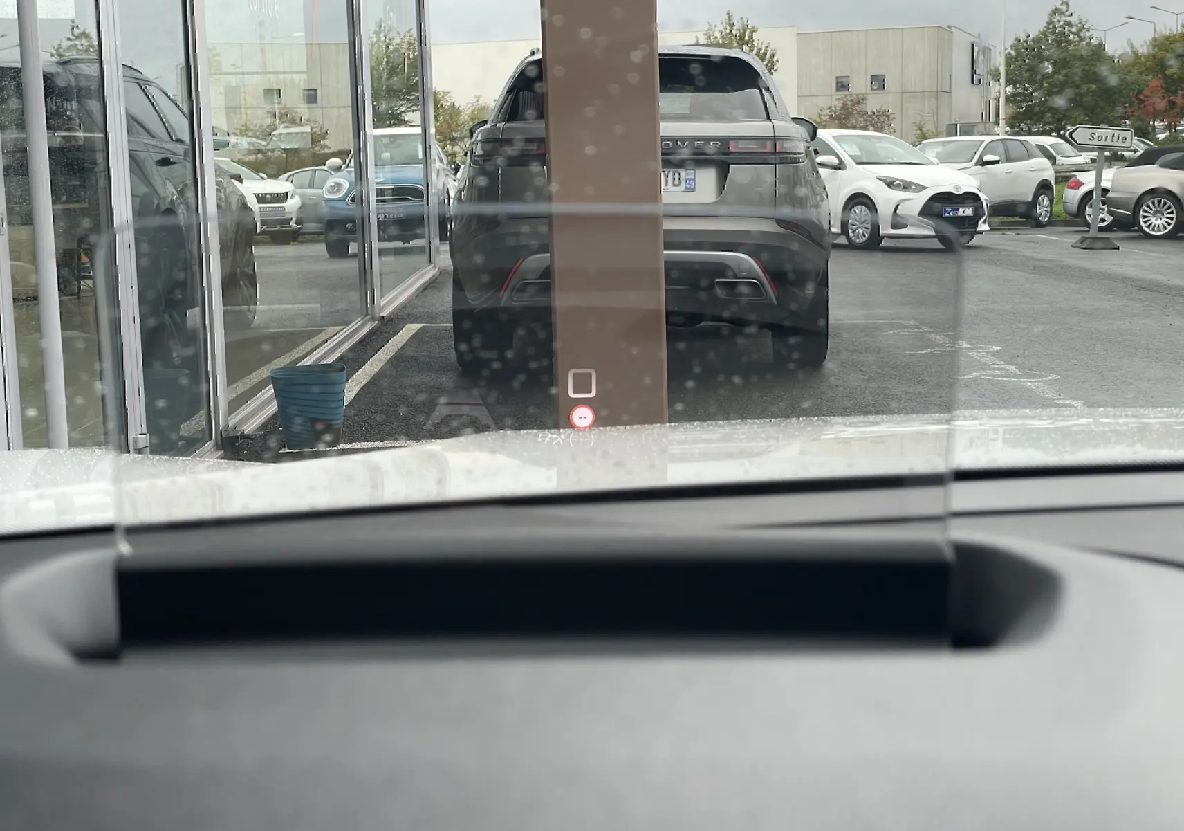 Vue depuis l'habitacle d'une Citroën C4 blanche, avec un SUV gris en arrière-plan et un panneau "Sortie" visible.