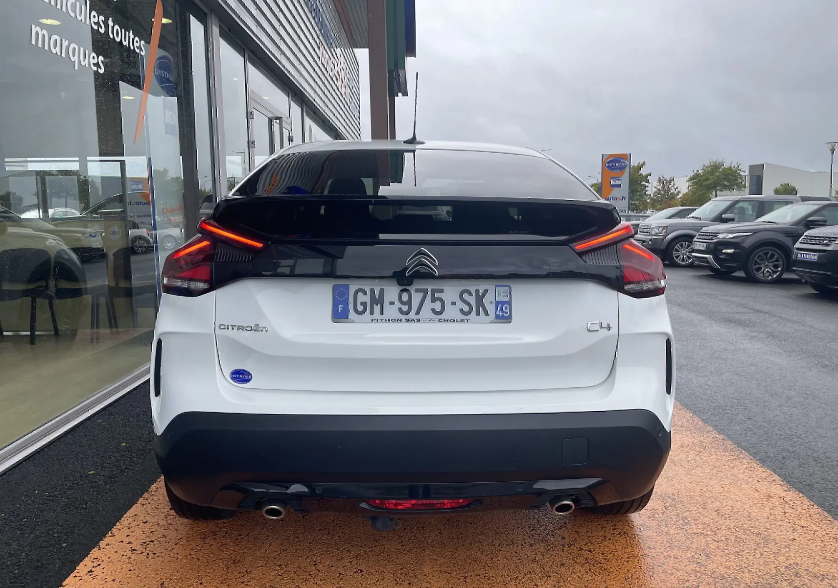 Vue arrière d'une Citroën C4 blanche 2022 avec feux LED allumés et toit noir brillant sur parking.