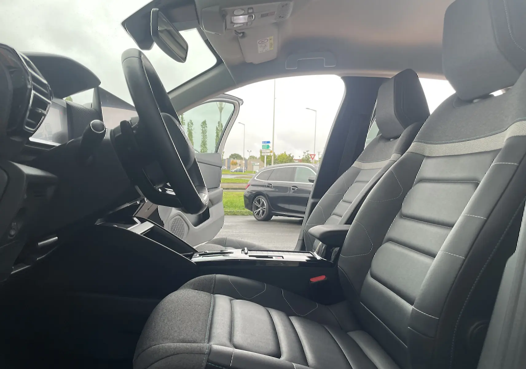 Vue intérieure côté conducteur de la Citroën C4 blanche 2022, sièges tissu gris noir et volant multifonction.