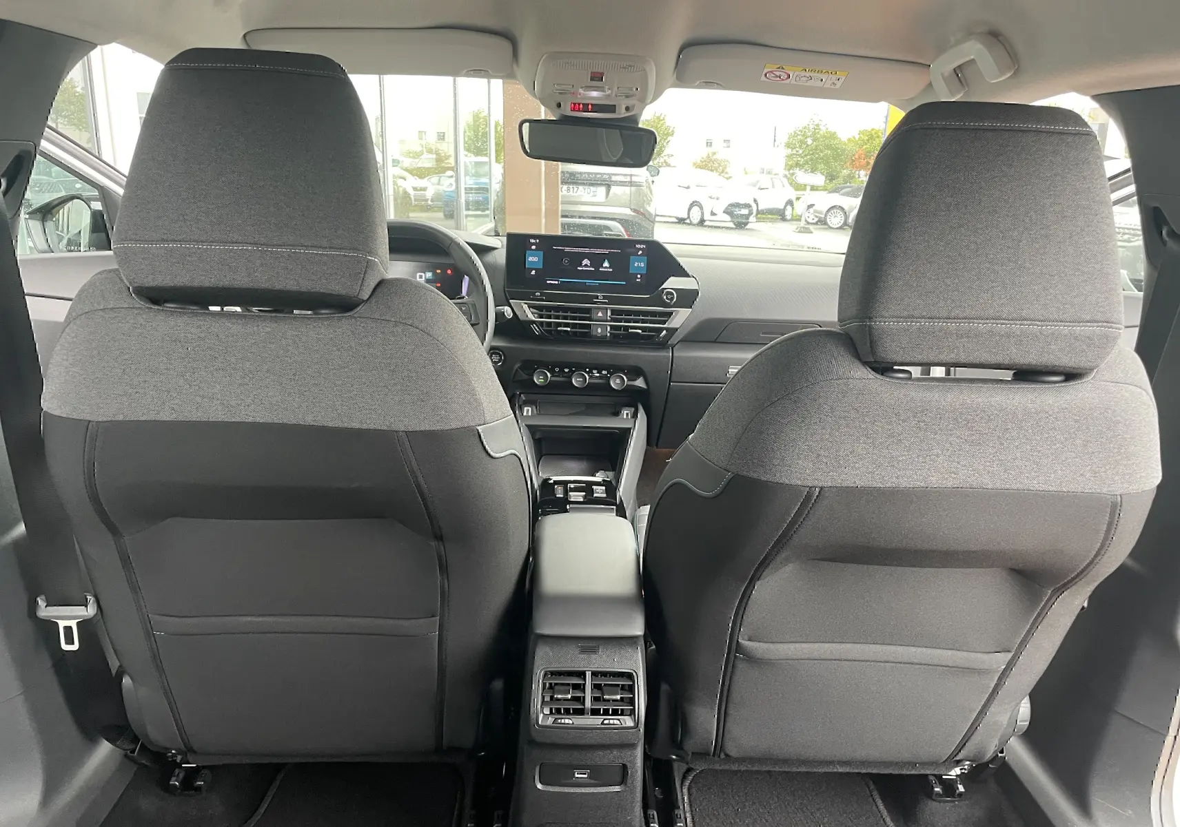 Vue arrière de l'intérieur d'une Citroën C4 blanche 2022, sièges en tissu gris noir et tableau de bord moderne avec écran tactile.